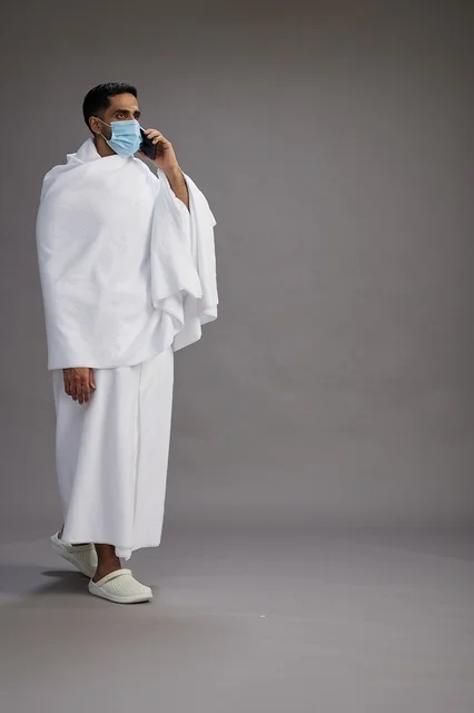 Saudi Pilgrim in Ihram with Mask Using Smartphone