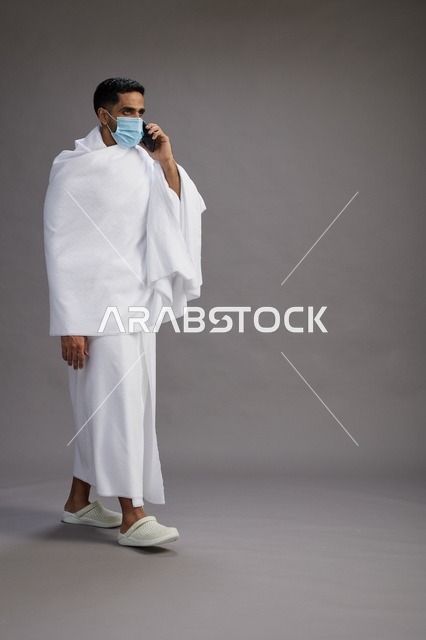 رجل سعودي بملابس الإحرام والكمامة يستخدم الهاتف