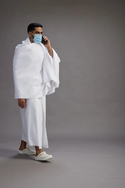 رجل سعودي بملابس الإحرام والكمامة يستخدم الهاتف