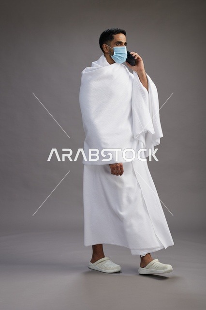 حاج سعودي بملابس الإحرام يرتدي كمامة ويستخدم الجوال