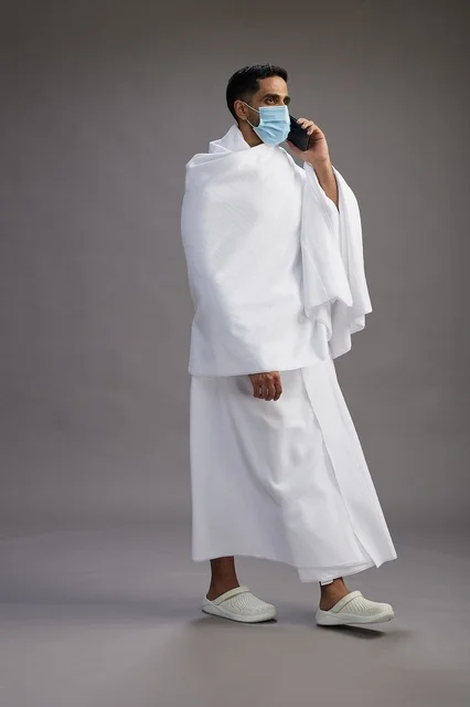 حاج سعودي بملابس الإحرام يرتدي كمامة ويستخدم الجوال