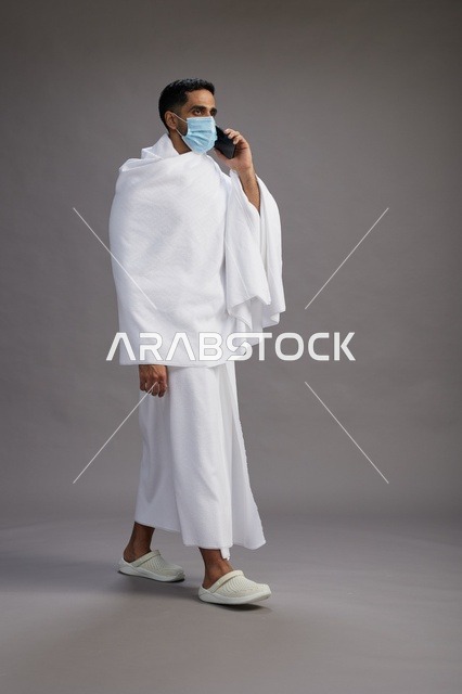 رجل سعودي بملابس الإحرام والكمامة يتحدث بالهاتف
