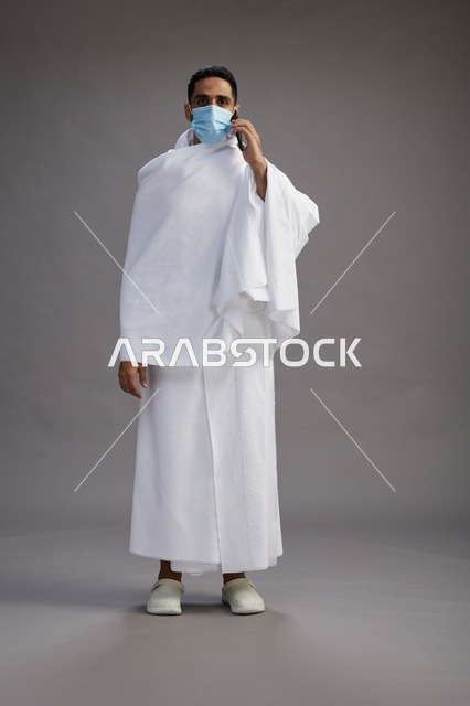 معتمر سعودي بملابس الإحرام والكمامة مع هاتف ذكي
