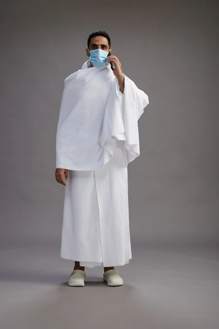 معتمر سعودي بملابس الإحرام والكمامة مع هاتف ذكي