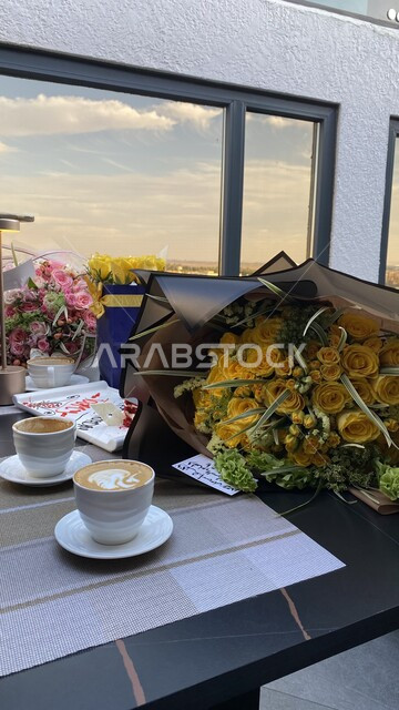 صورة لفناجين القهوة وبوكيه الورد الاصفر على الطاولة  في أحد الكافيهات ، مناسبة سعيدة  ، جلسة هادئة في مقهى سعودي 