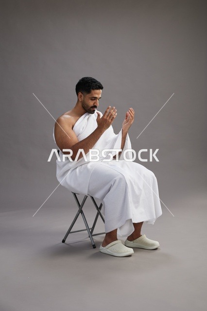 حاج سعودي يرتدي ملابس الإحرام ويجلس للدعاء في الاستوديو