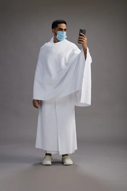 حاج سعودي بملابس الإحرام يجري مكالمة فيديو بالكمامة