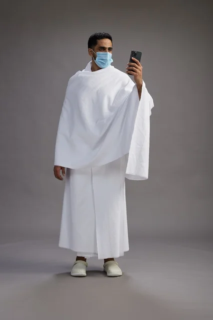 حاج سعودي بملابس الإحرام يجري مكالمة فيديو بالكمامة