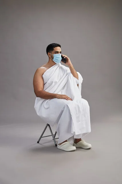 Saudi man in ihram sitting with face mask while on a phone call