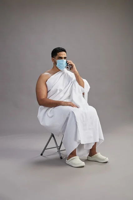Saudi man in ihram sitting with face mask while on a phone call