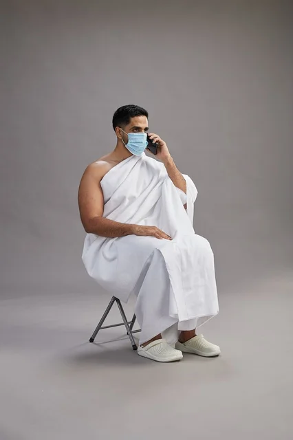 Saudi man in ihram sitting with face mask while on a phone call Saudi man in ihram sitting with face mask while on a phone call