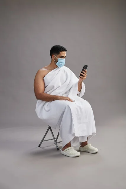 Saudi man in ihram sitting and using smartphone with face mask
