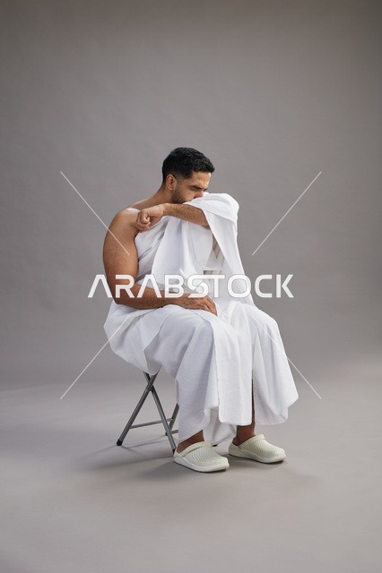 رجل سعودي بملابس الإحرام يعطس في استوديو بخلفية رمادية