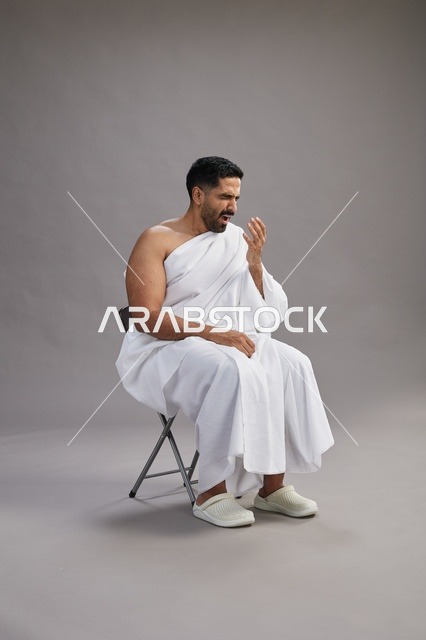 رجل سعودي بملابس الإحرام يعطس في استوديو خلفية رمادية