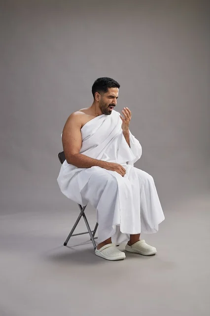 Saudi Man in Ihram Sneezing Against Grey Background