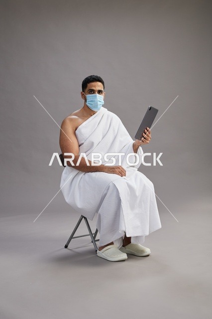 Saudi Man in Ihram Using Tablet and Wearing Mask