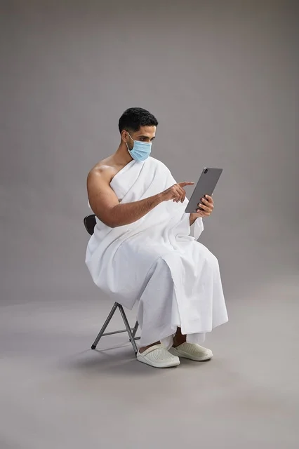 Saudi Pilgrim in Ihram Using Tablet with Face Mask