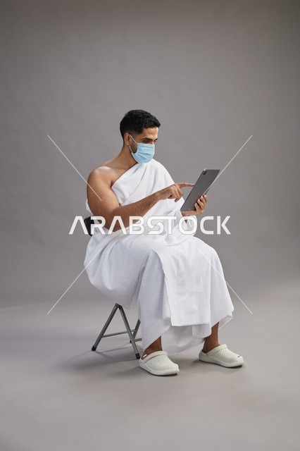 رجل سعودي بملابس الإحرام يستخدم تابلت مع كمامة