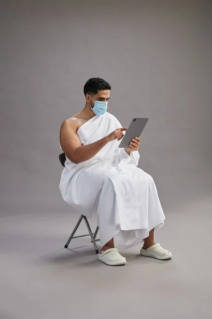 Saudi Man in Ihram Using Tablet with Medical Mask