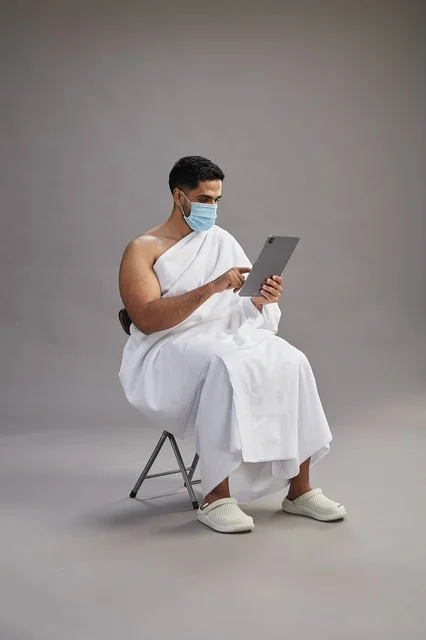 Saudi Man in Ihram Using Tablet with Face Mask