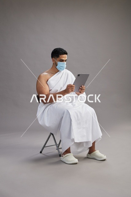 Saudi Man in Ihram Using Tablet with Face Mask