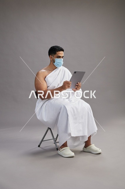 Saudi Man in Ihram Using Tablet with Face Mask