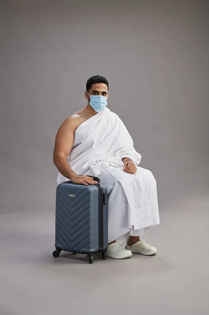 رجل سعودي بملابس الإحرام مع حقيبة سفر وكمامة طبية