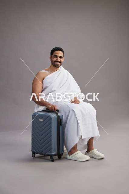 رجل سعودي بملابس الإحرام يجلس مع حقيبة سفر