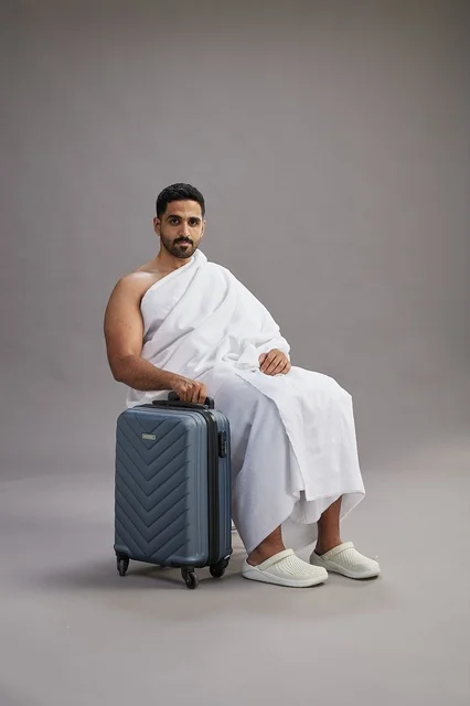 رجل سعودي بملابس الإحرام يجلس مع حقيبة سفر