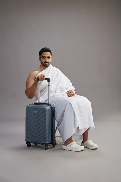 رجل سعودي بملابس الإحرام يجلس مع حقيبة سفر