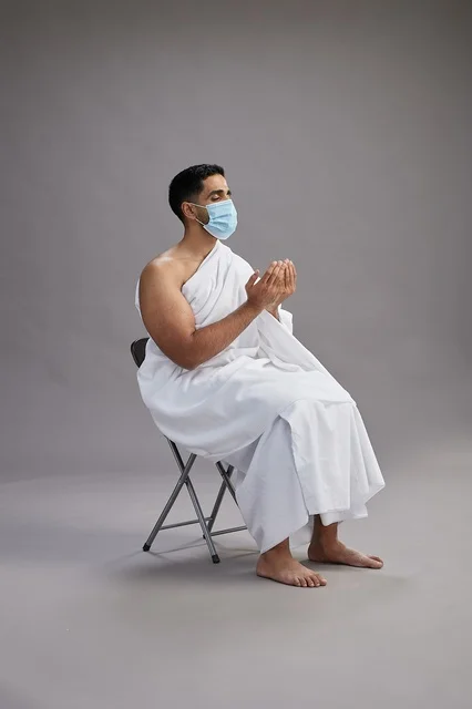 رجل سعودي بملابس الإحرام يرتدي كمامة ويؤدي الدعاء