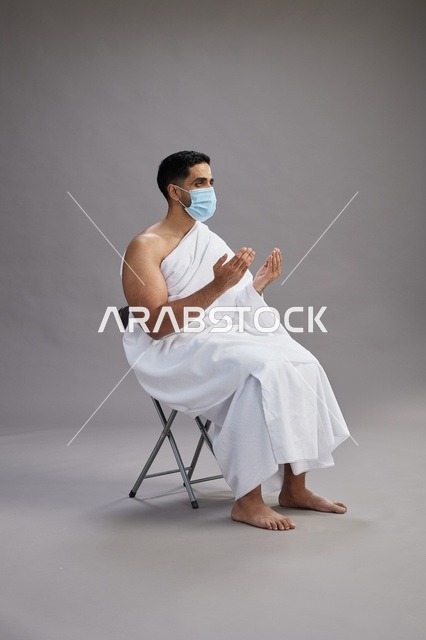 رجل سعودي بملابس الإحرام يدعو ويرتدي كمامة طبية