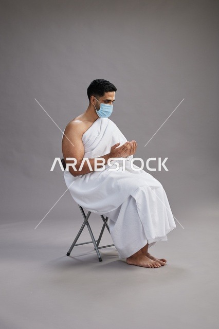 رجل سعودي بملابس الإحرام يرتدي كمامة ويدعو