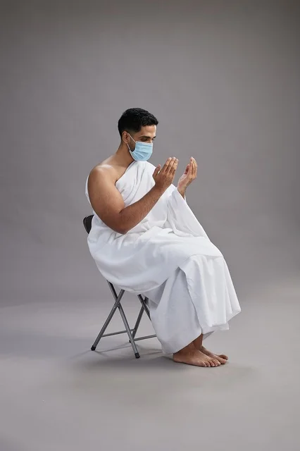 رجل سعودي بملابس الإحرام والكمامة أثناء الدعاء
