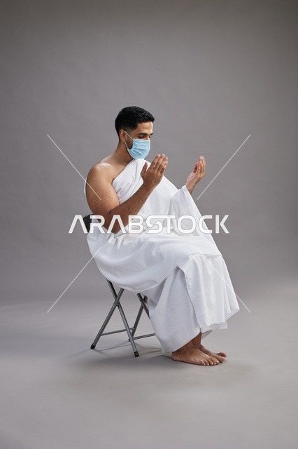 رجل سعودي بملابس الإحرام والكمامة يدعو في استوديو