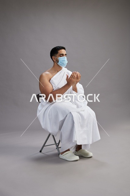 رجل سعودي بملابس الإحرام يدعو ويرتدي كمامة