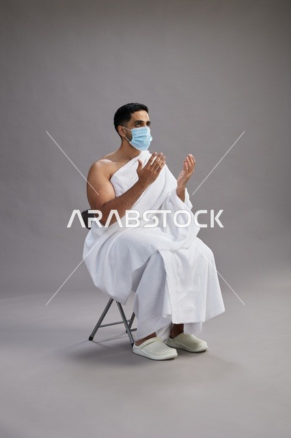 رجل سعودي بملابس الإحرام والكمامة يدعو في الاستوديو