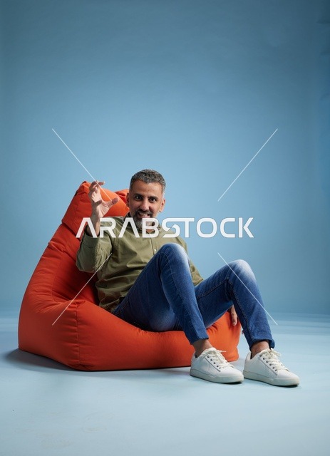 رجل يجلس على كرسي بين باج برتقالي بخلفية زرقاء
