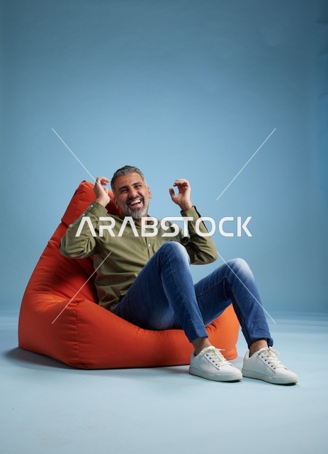 رجل في منتصف العمر يضحك جالساً على كرسي بين باج أحمر