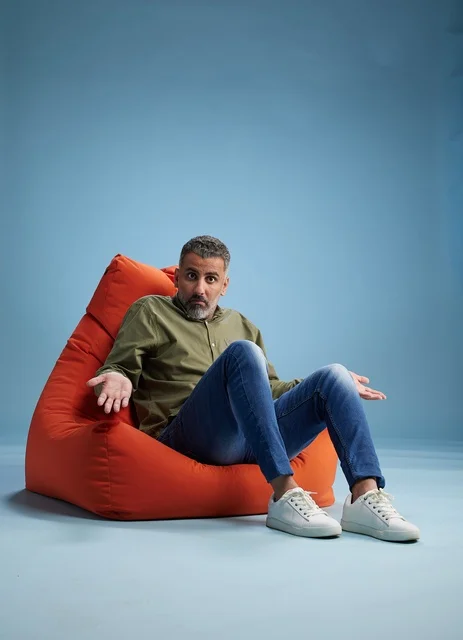 Man Sitting on Red Beanbag Shrugging on Blue Background