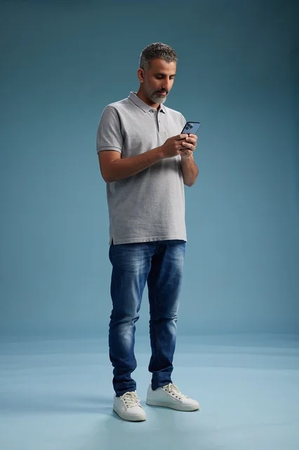 رجل سعودي يستخدم الهاتف الذكي بخلفية استوديو زرقاء