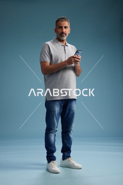 رجل عربي يمسك هاتف ذكي في الاستوديو بخلفية زرقاء