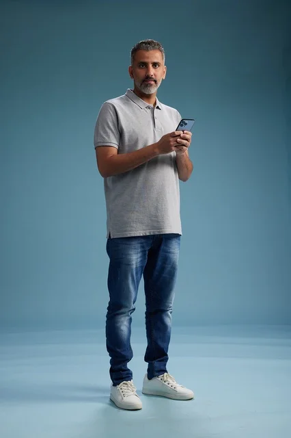رجل عربي يمسك هاتف ذكي في الاستوديو بخلفية زرقاء