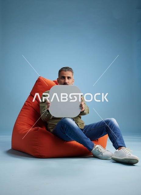 رجل سعودي يجلس على مقعد برتقالي يحمل لافتة فارغة