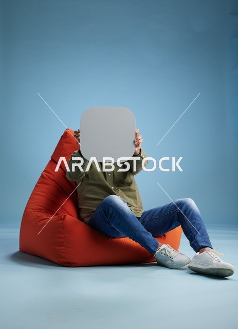 رجل سعودي على مقعد أحمر يحمل لوحة فارغة