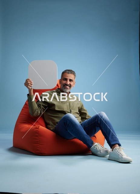 رجل سعودي يحمل لافتة بيضاء فارغة على كرسي بين باج أحمر
