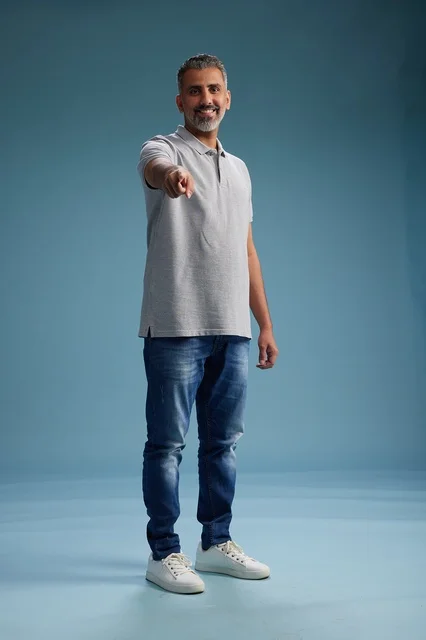 رجل سعودي يشير للكاميرا بملابس كاجوال