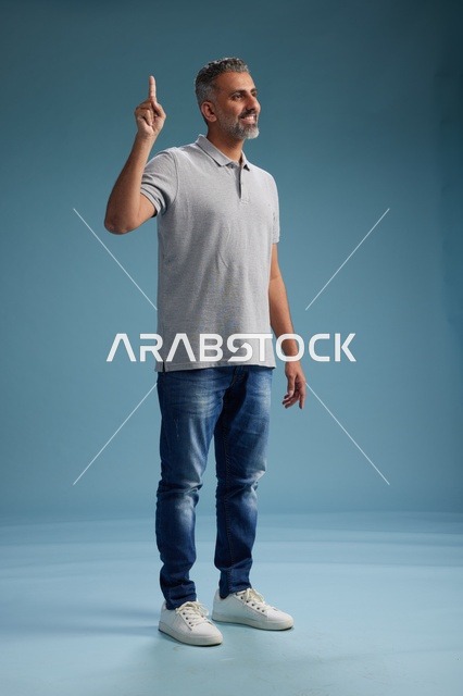 رجل سعودي بملابس كاجوال يشير للأعلى بخلفية زرقاء