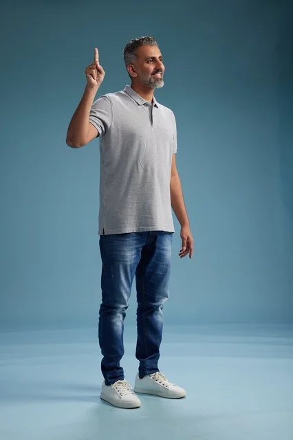 رجل سعودي بملابس كاجوال يشير للأعلى بخلفية زرقاء