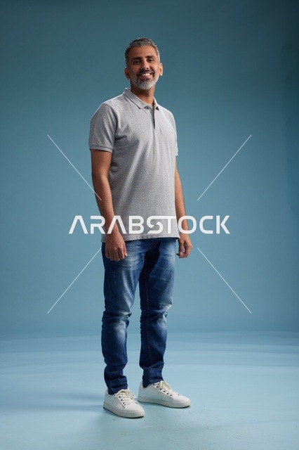رجل سعودي بملابس كاجوال يقف في استوديو بخلفية زرقاء